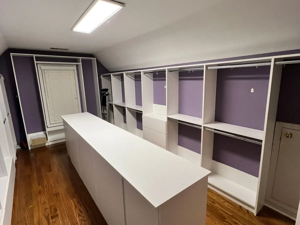 Custom walk-in closet with wood shelving, drawers, and hanging space by Pi Cabinetry